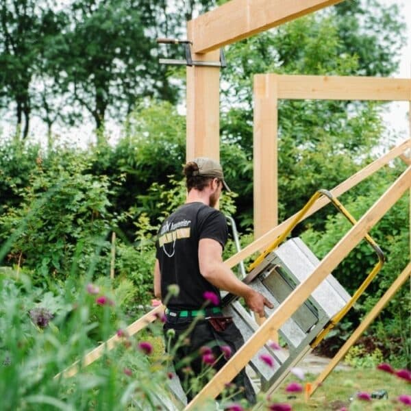 DIM-vakman bouwt een houten pergola op in een bloemrijke tuin