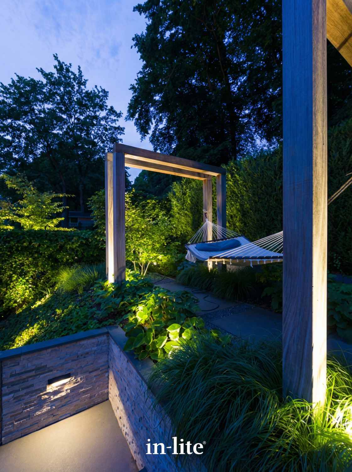 Moderne tuinverlichting in strakke achtertuin met houten pergola, sfeervolle LED spots tussen beplanting en wandverlichting bij trap in avondschemering.